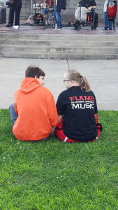 Two individuals sitting on the grass in front of a band playing